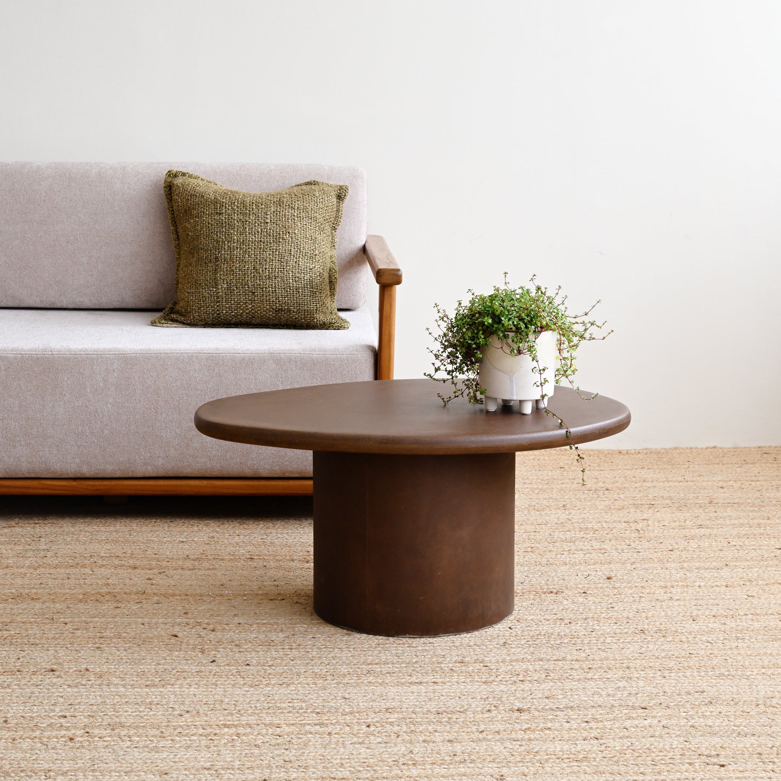 Sofa with a pillow and a round wooden table in a room with a white wall and beige carpet.