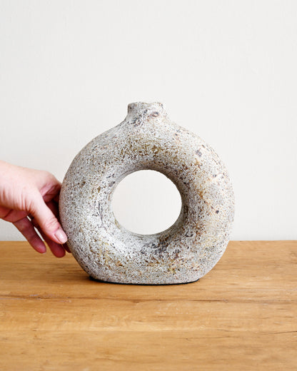 Hand holding a textured ceramic vase on a wooden surface with a white background