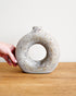 Hand holding a textured ceramic vase on a wooden surface with a white background