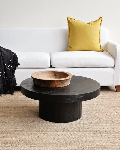 Black round coffee table with a wooden bowl in a living room setting.