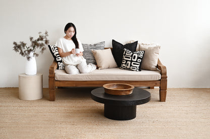 Woman sitting on a wooden sofa with decorative pillows in a minimalistic living room.