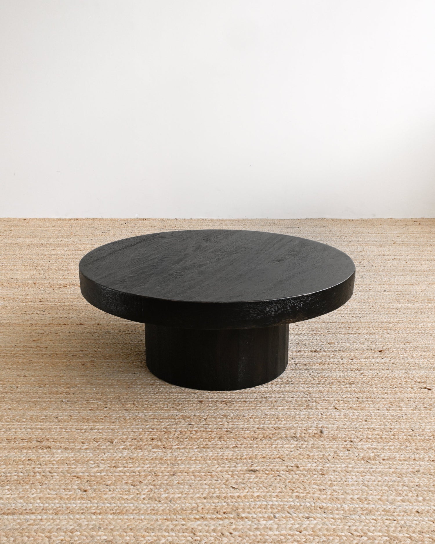 Round black stone table on a beige carpet with a white wall background