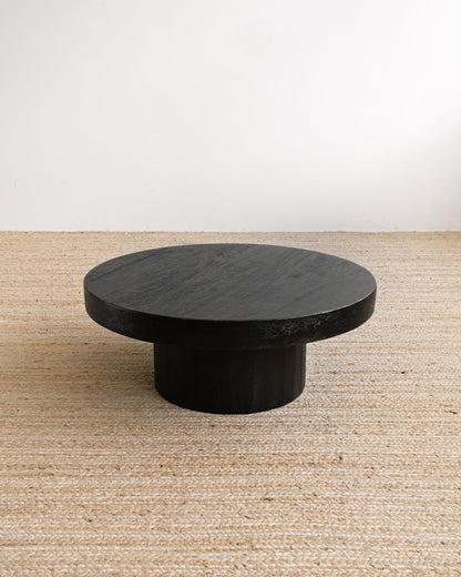 Round black stone table on a beige carpet with a white wall background