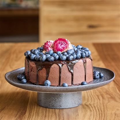 Chocolate cake with blueberries and pink flowers on a wooden table
