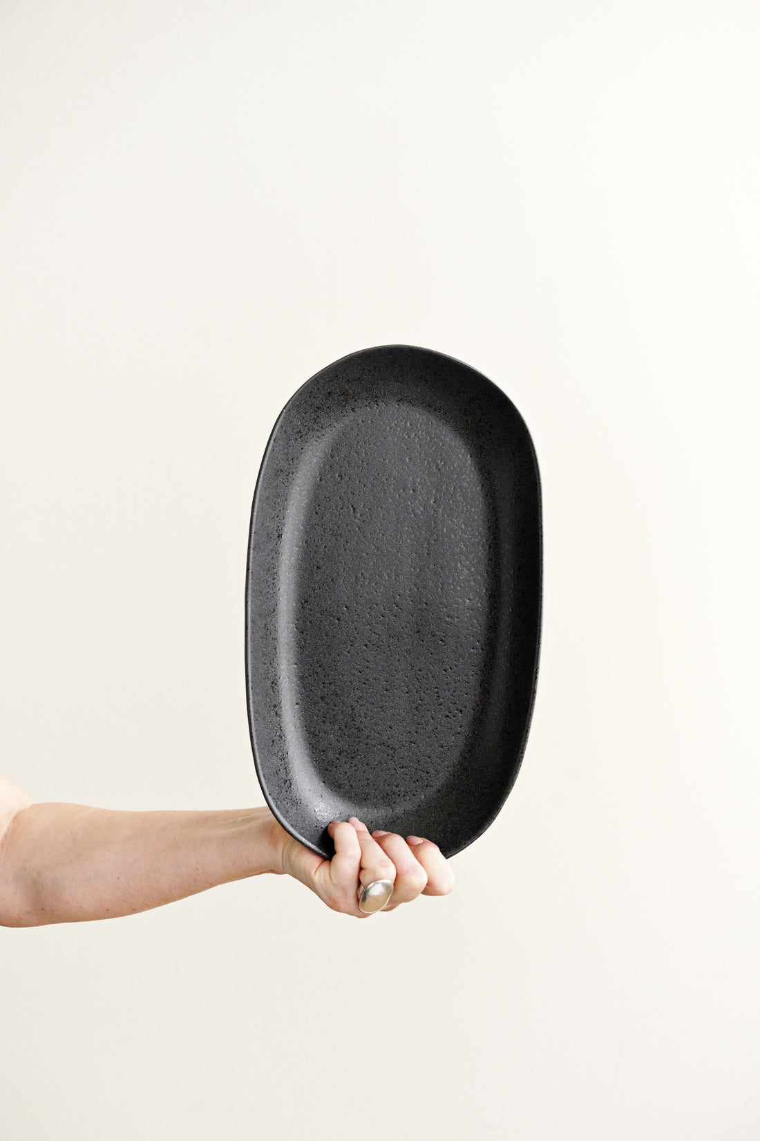 Person holding a black oval plate against a white background