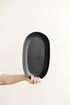 Person holding a black oval plate against a white background