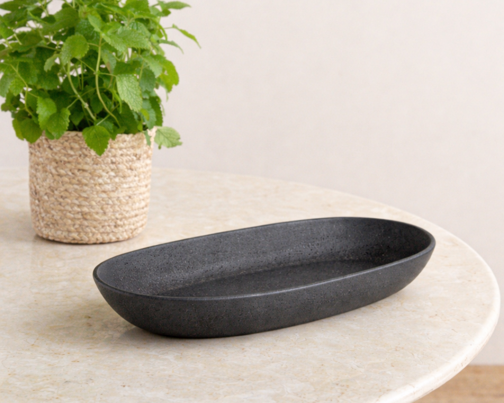 Black oval dish on a light-colored surface with a green plant in the background