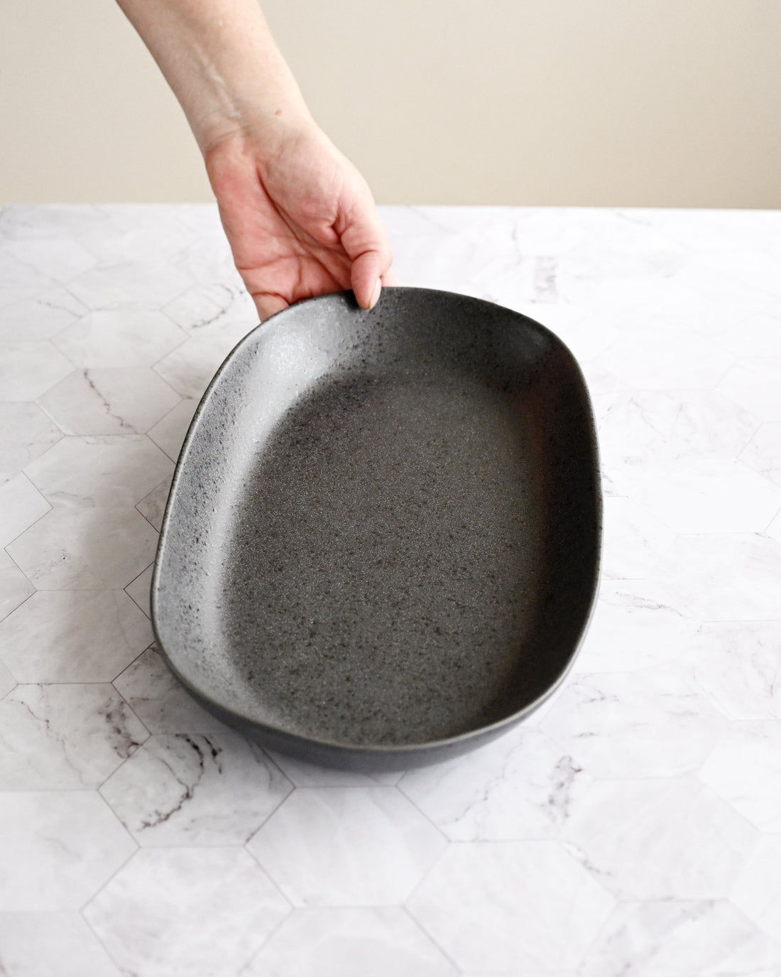 Person holding a black ceramic dish on a marble surface