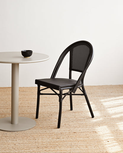 Black chair next to a round white table on a light wooden floor with a white wall background