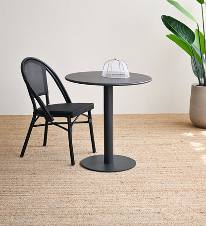 Black chair and table set with a plant on a wooden floor against a white wall