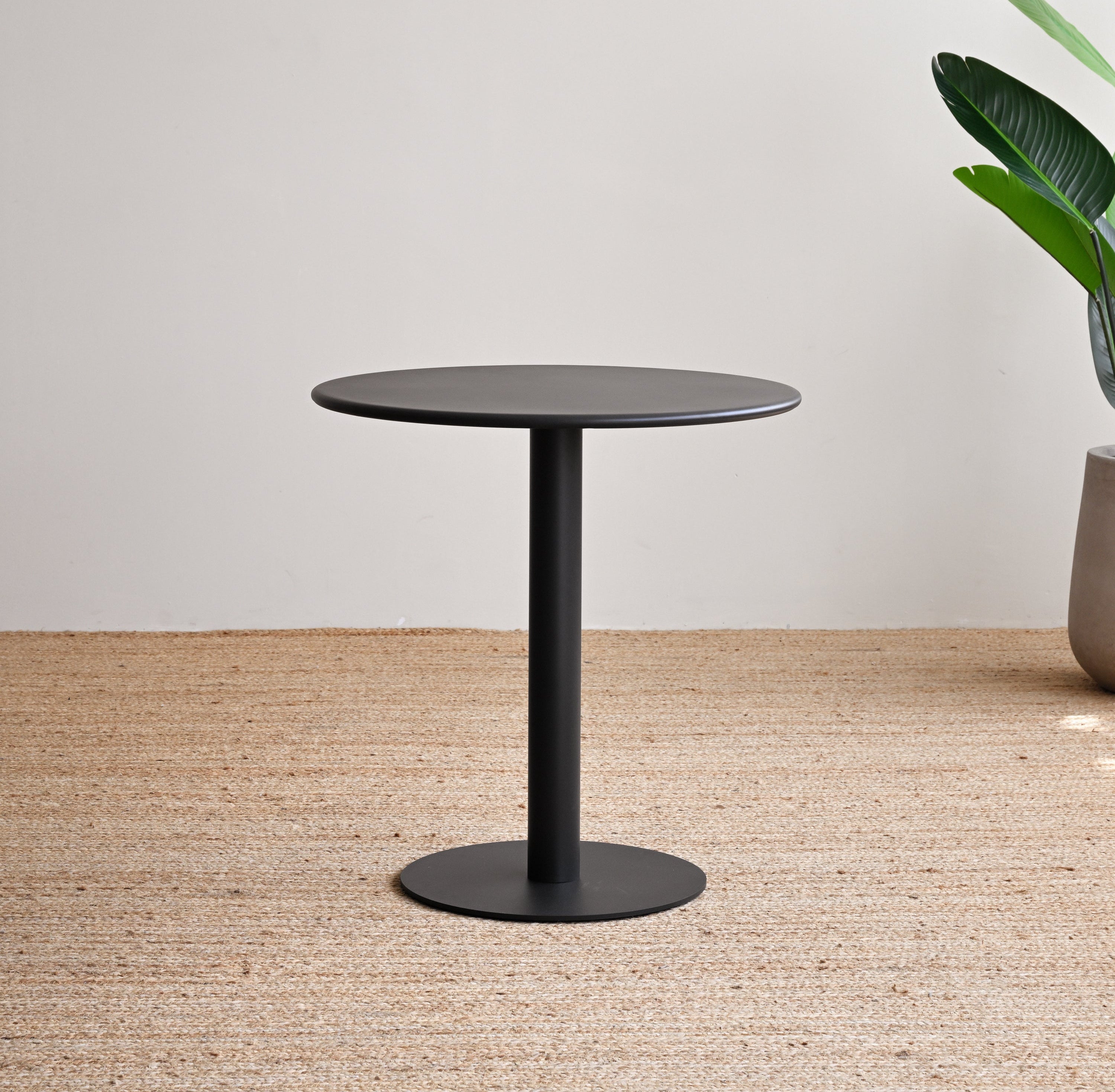 Black round table on a textured floor with a plant in the background