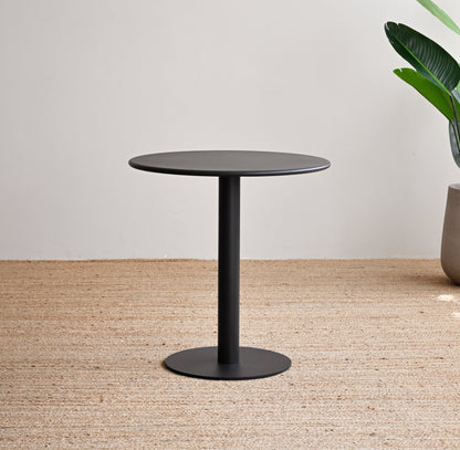 Black round table on a textured floor with a plant in the background