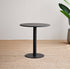 Black round table on a textured floor with a plant in the background
