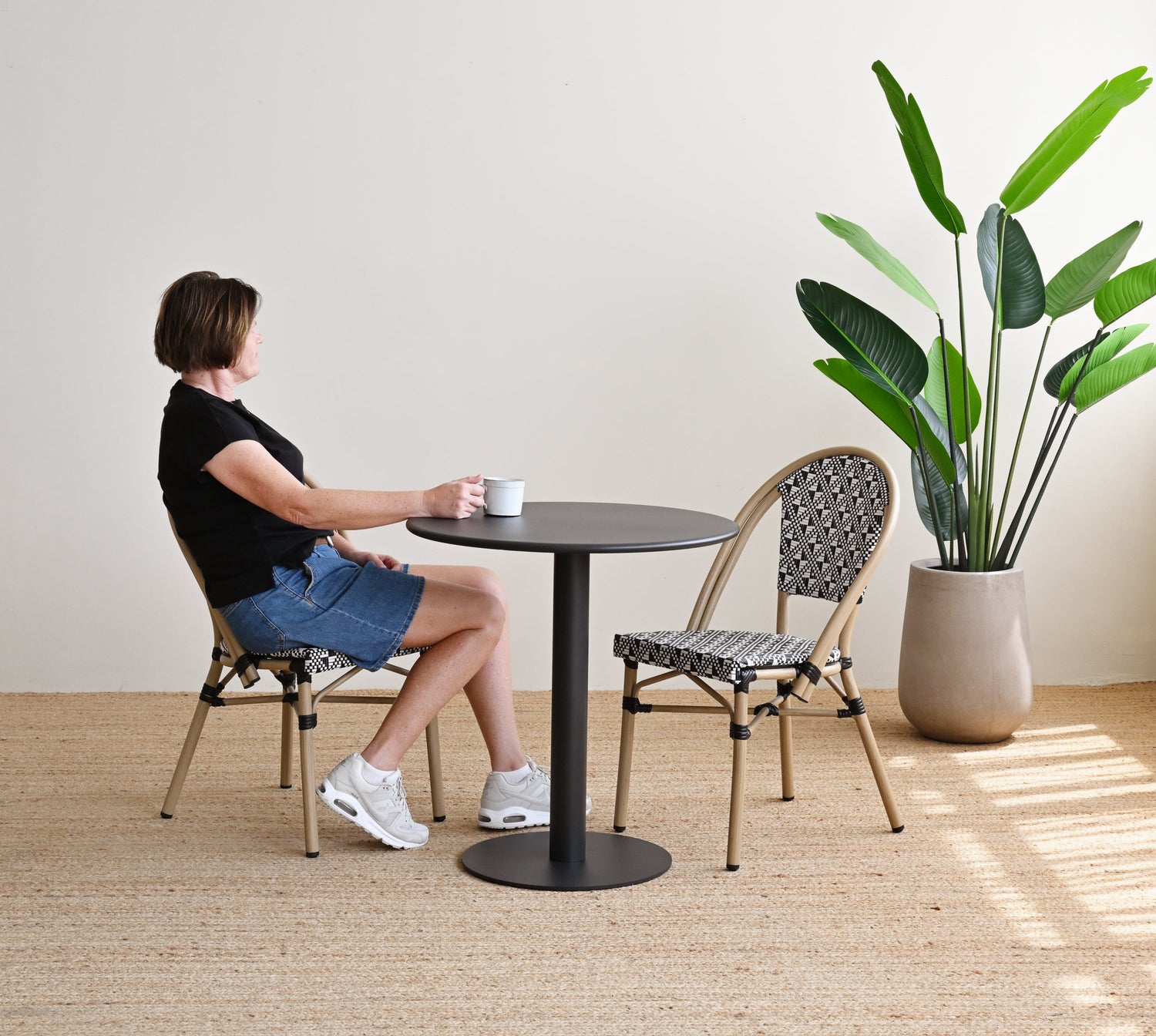 Woman sitting at a small round table with a plant in the background