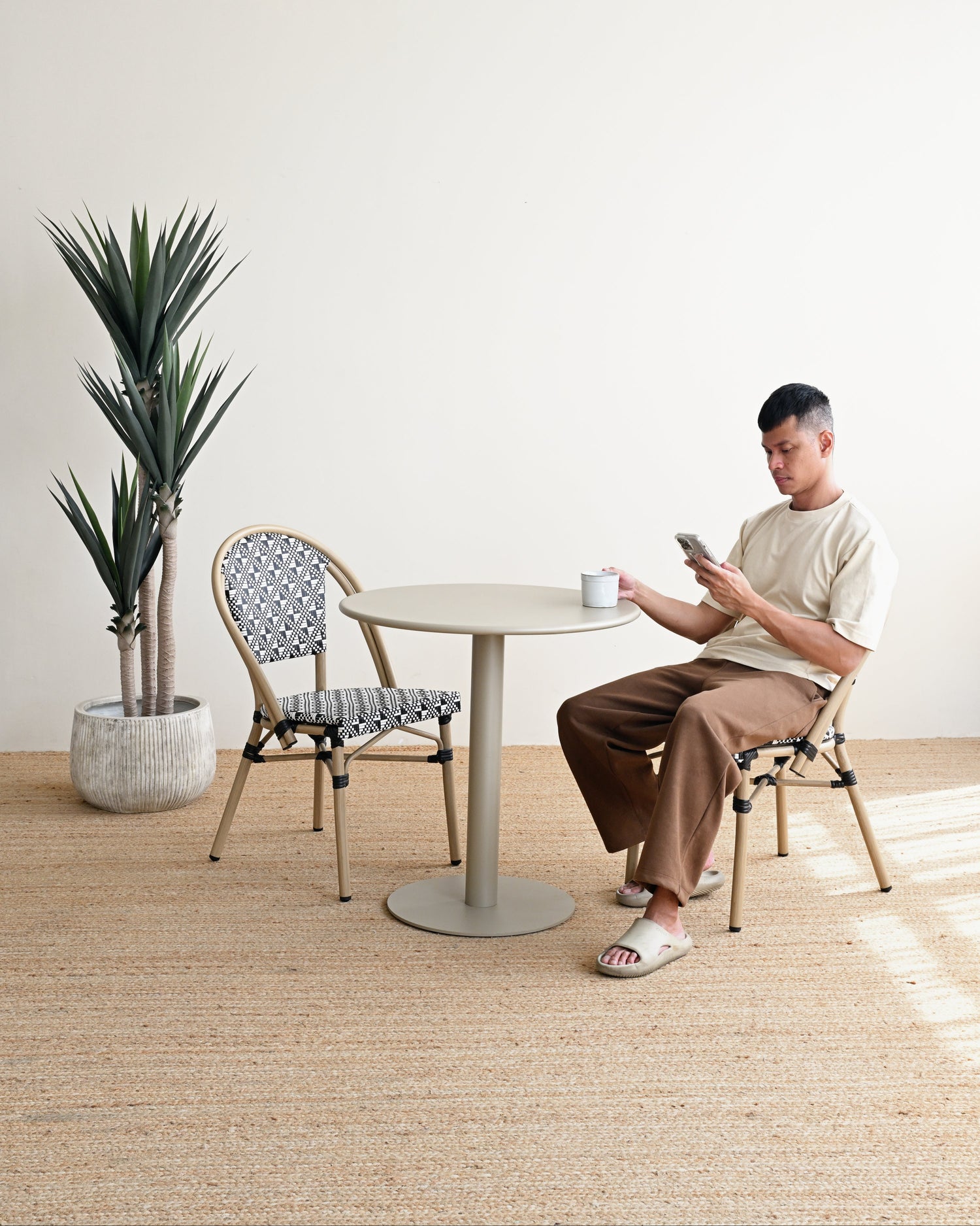 Man sitting at a table with a plant and chair in a minimalistic room.