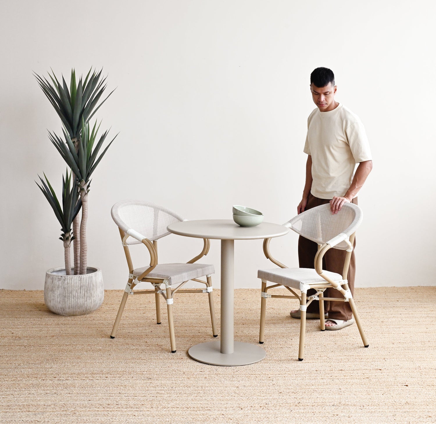 Man standing in a minimalistic room with a round table and chairs, a plant, and a white wall.