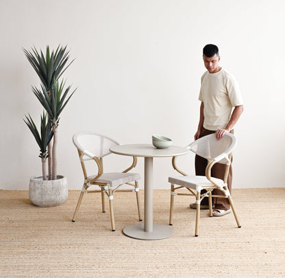 Man standing in a minimalistic room with a round table and chairs, a plant, and a white wall.