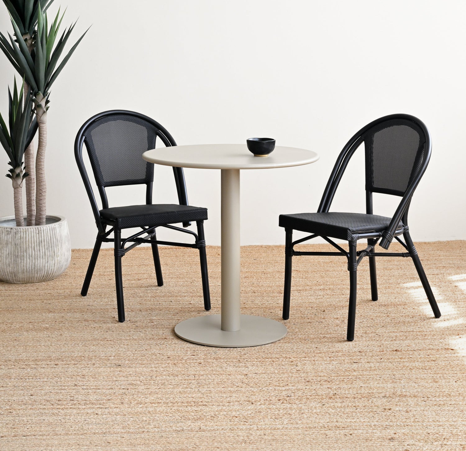 Round white table with two black chairs on a wooden floor.