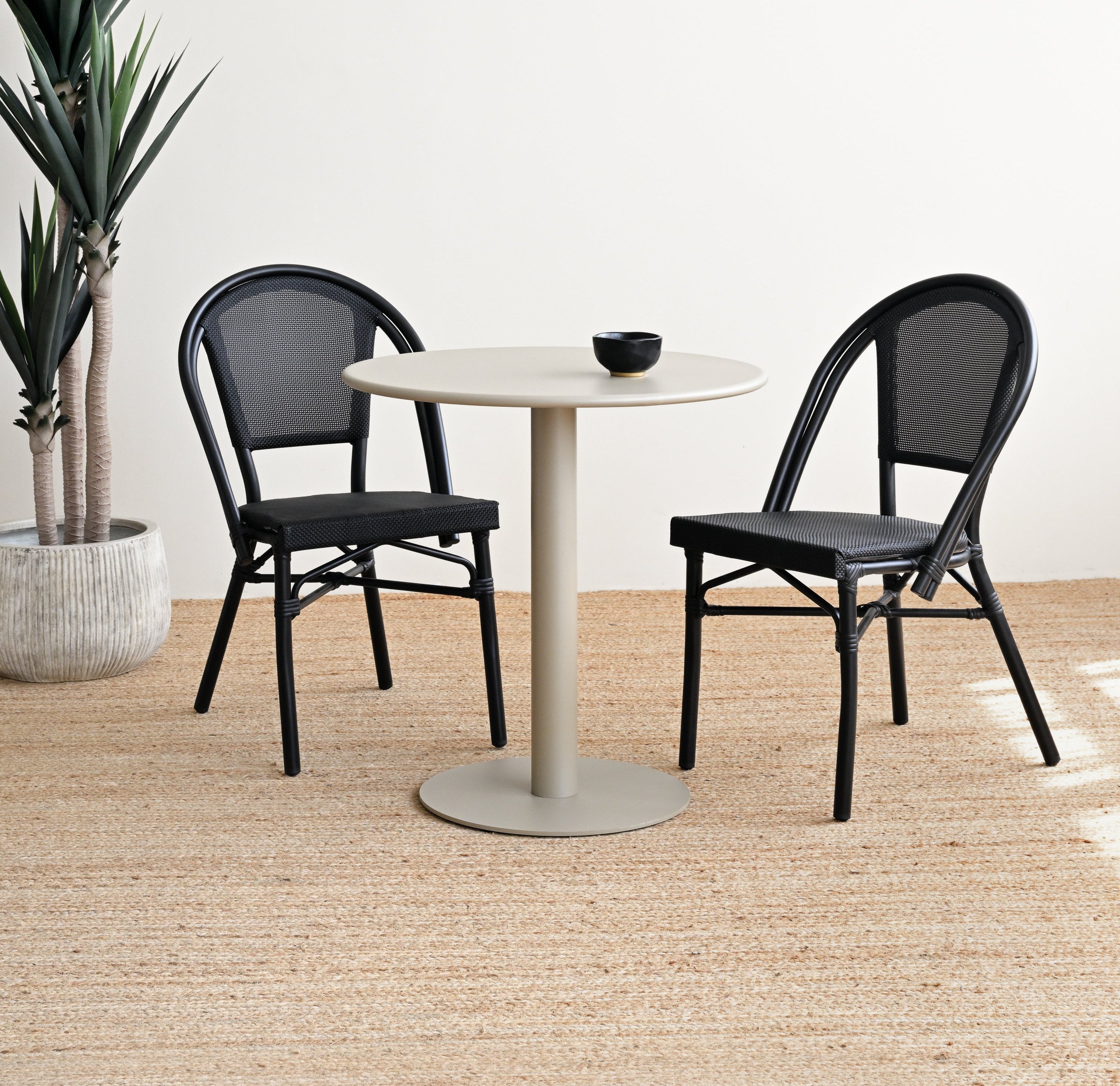 Round white table with two black chairs on a wooden floor.