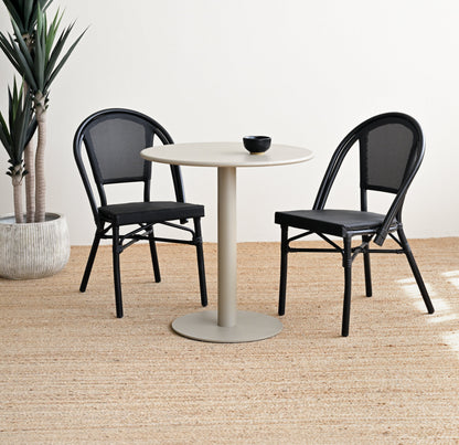 Round white table with two black chairs on a wooden floor.