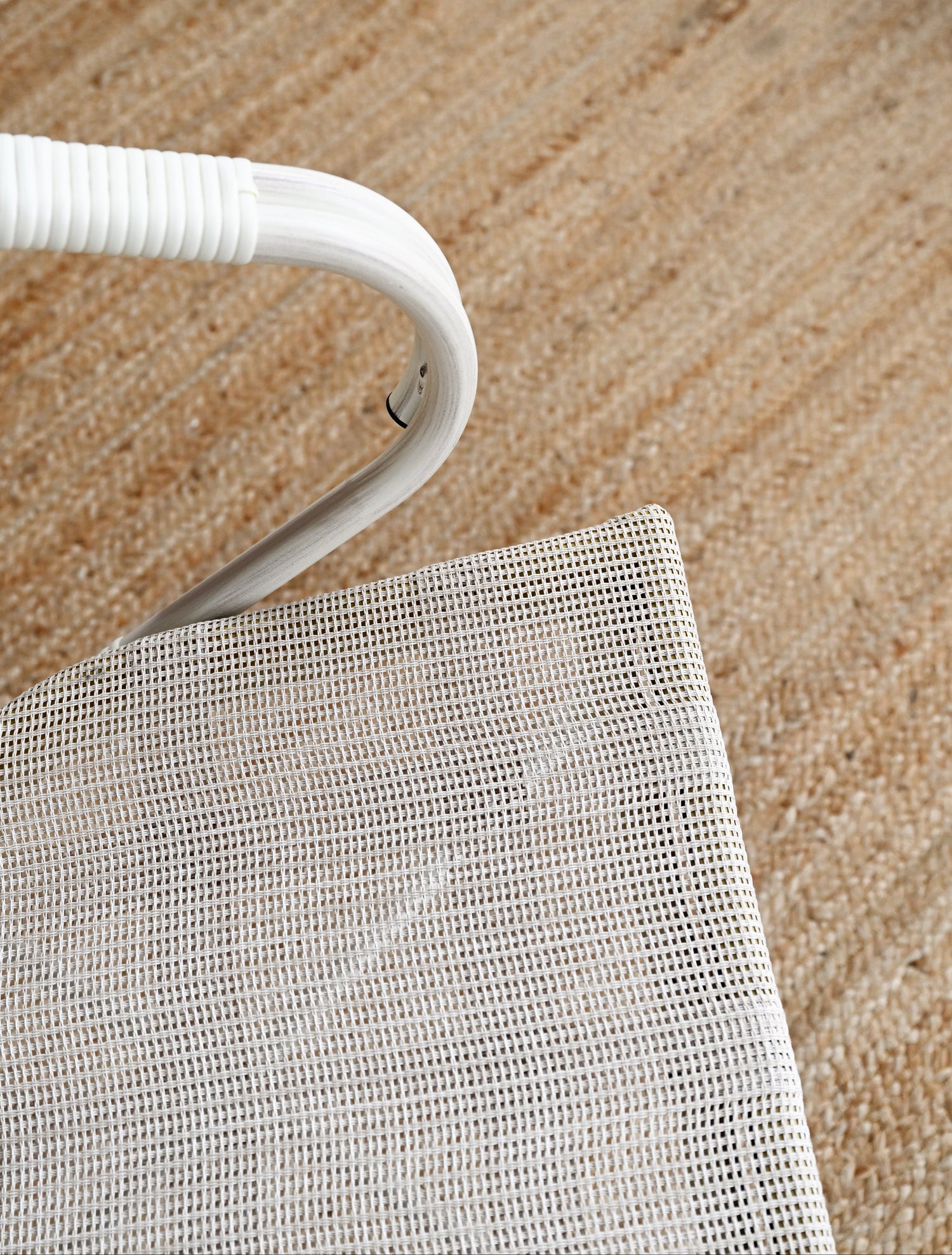 Close-up of a white chair with a mesh seat on a sandy surface