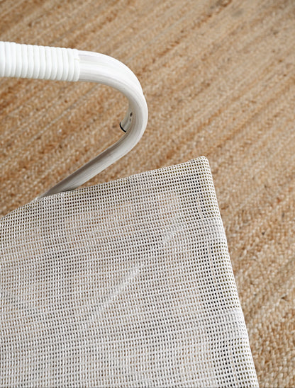 Close-up of a white chair with a mesh seat on a sandy surface