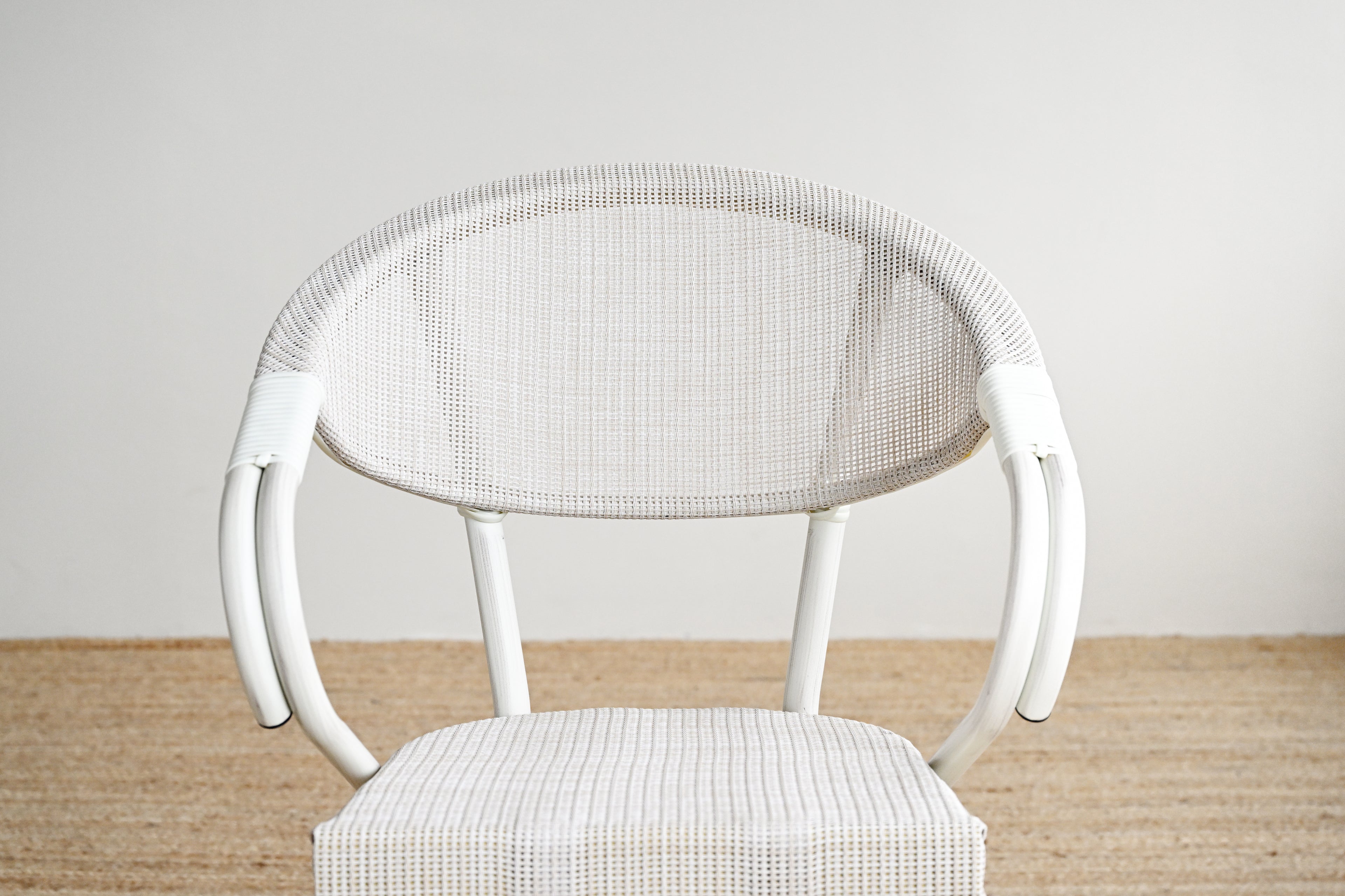 White wicker chair with a cushioned seat on a wooden floor against a white wall