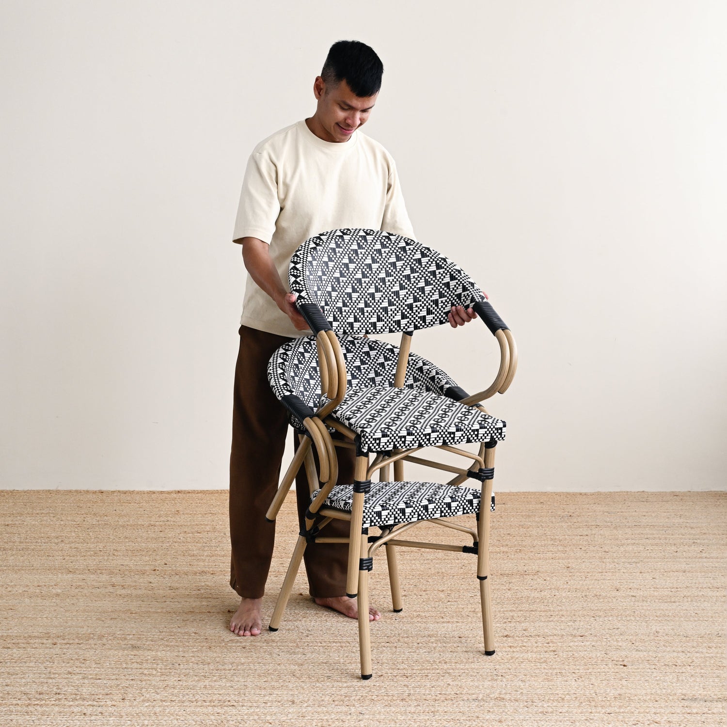 Person arranging patterned chairs on a wooden floor with a white wall background