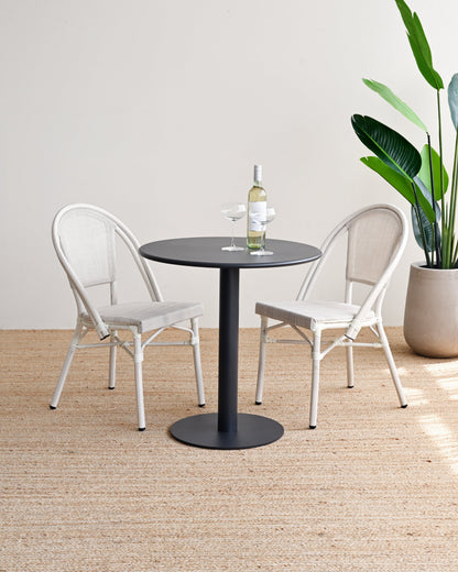 Two chairs around a round table with a plant in the corner on a wooden floor.