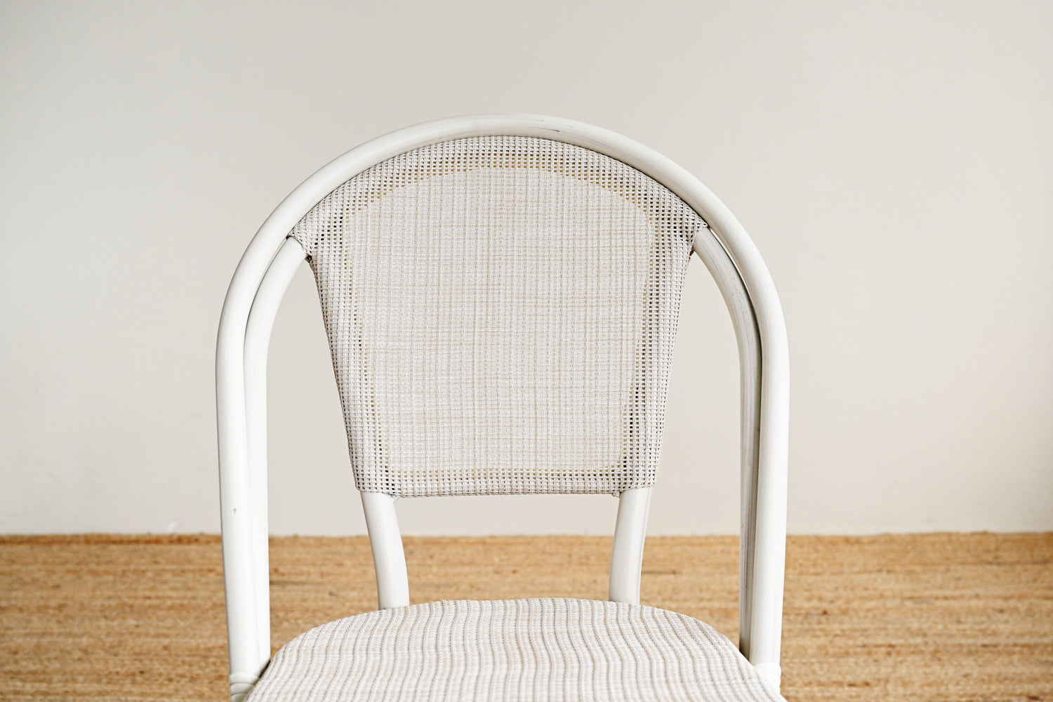White chair with woven backrest on a wooden floor against a plain wall