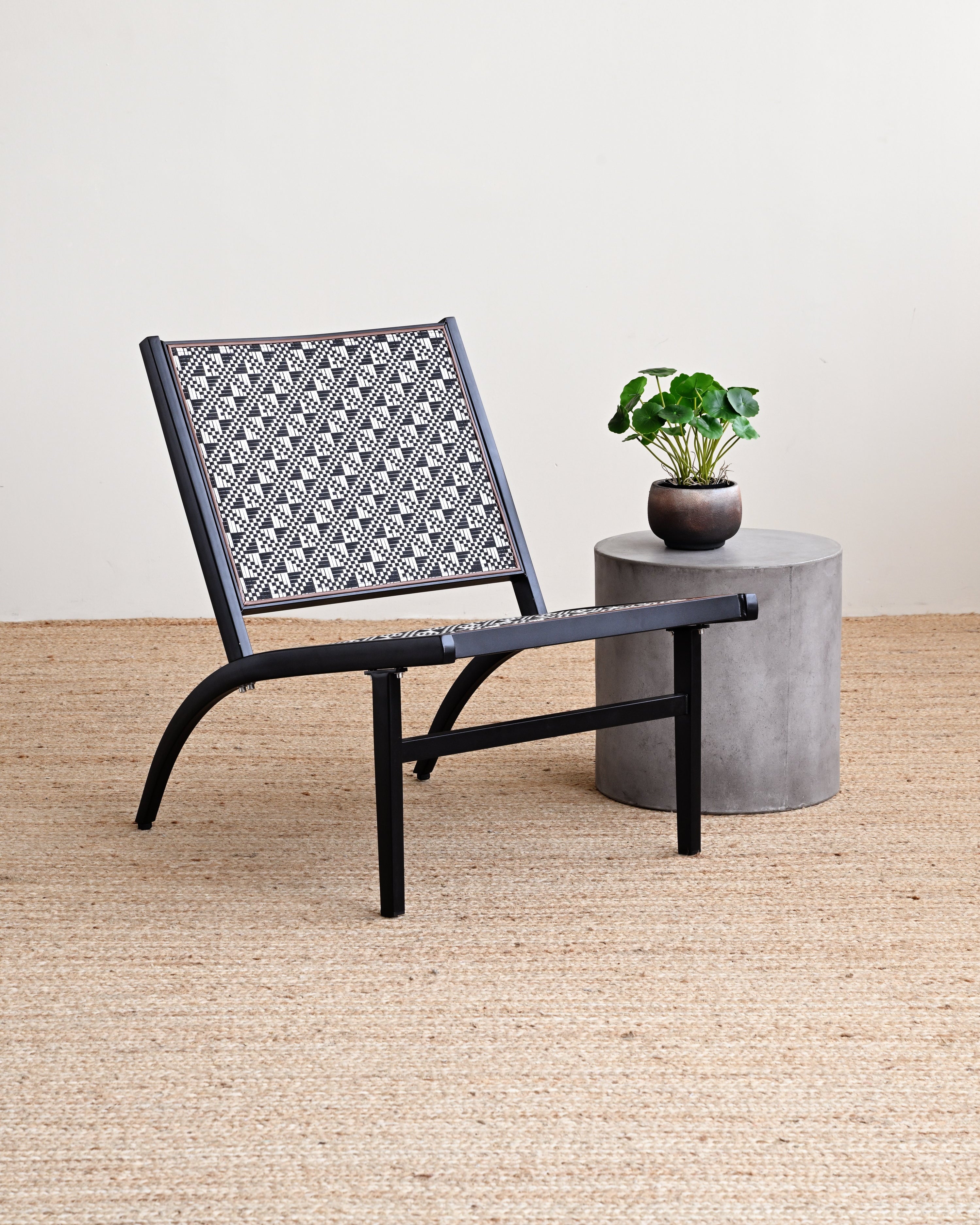 Black chair with patterned backrest next to a small concrete table with a plant on a beige carpet.