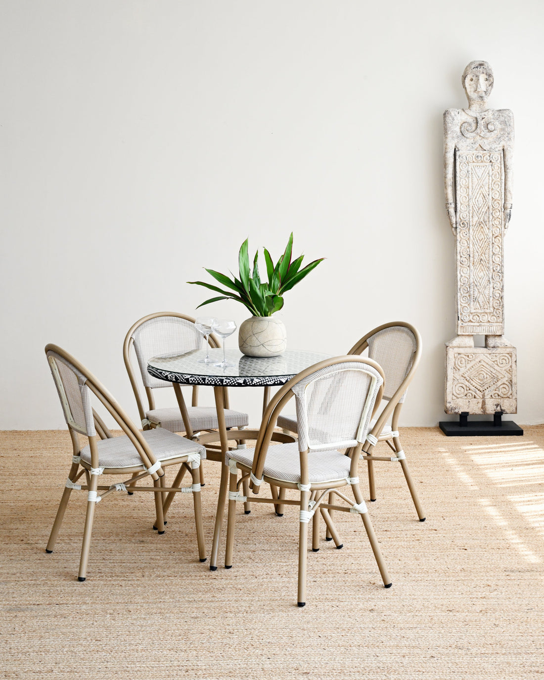 Dining area with round table and chairs in a room with a statue and plant.