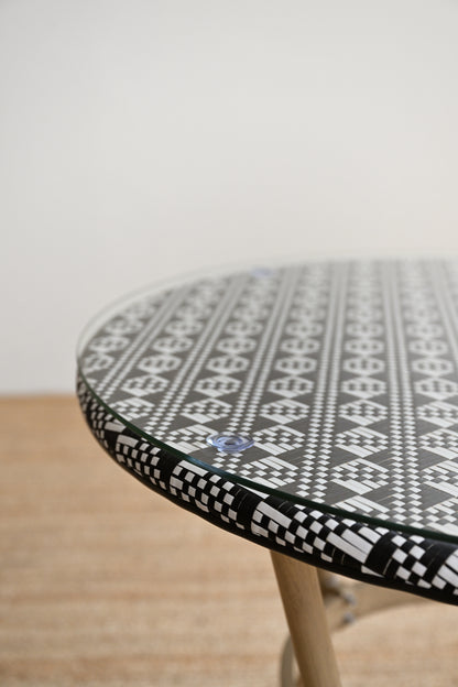 Round table with a black and white geometric pattern on a wooden floor.