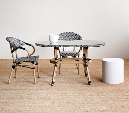 Round glass table with two chairs on a wooden floor against a white wall