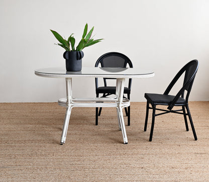 Round glass table with black chairs on a beige carpet against a white wall