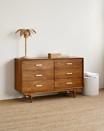 Wooden dresser with a lamp and box on top against a white wall.