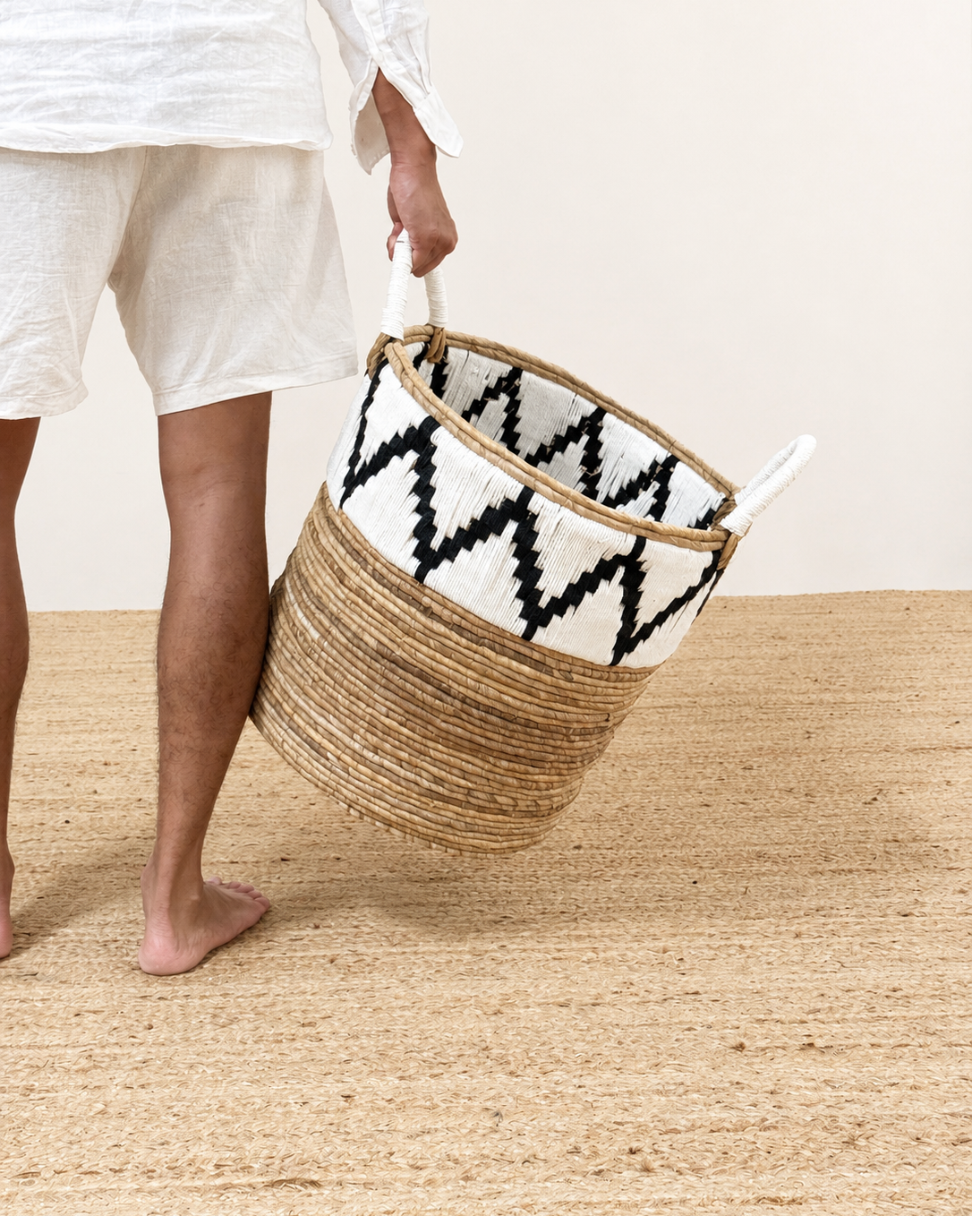 Person holding a woven basket with a black and white pattern on a wooden floor.