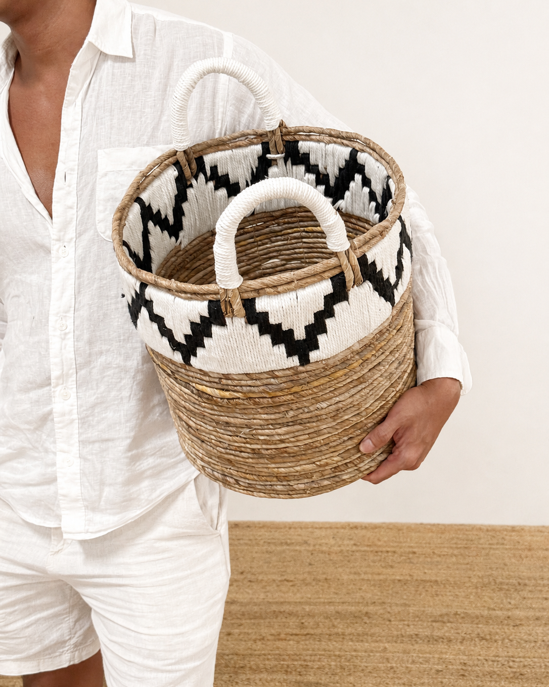 Person holding a woven basket with geometric pattern on a plain background