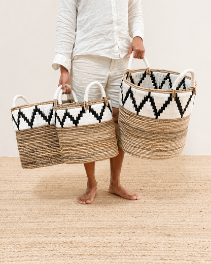 Person holding two woven baskets with geometric patterns on a neutral background