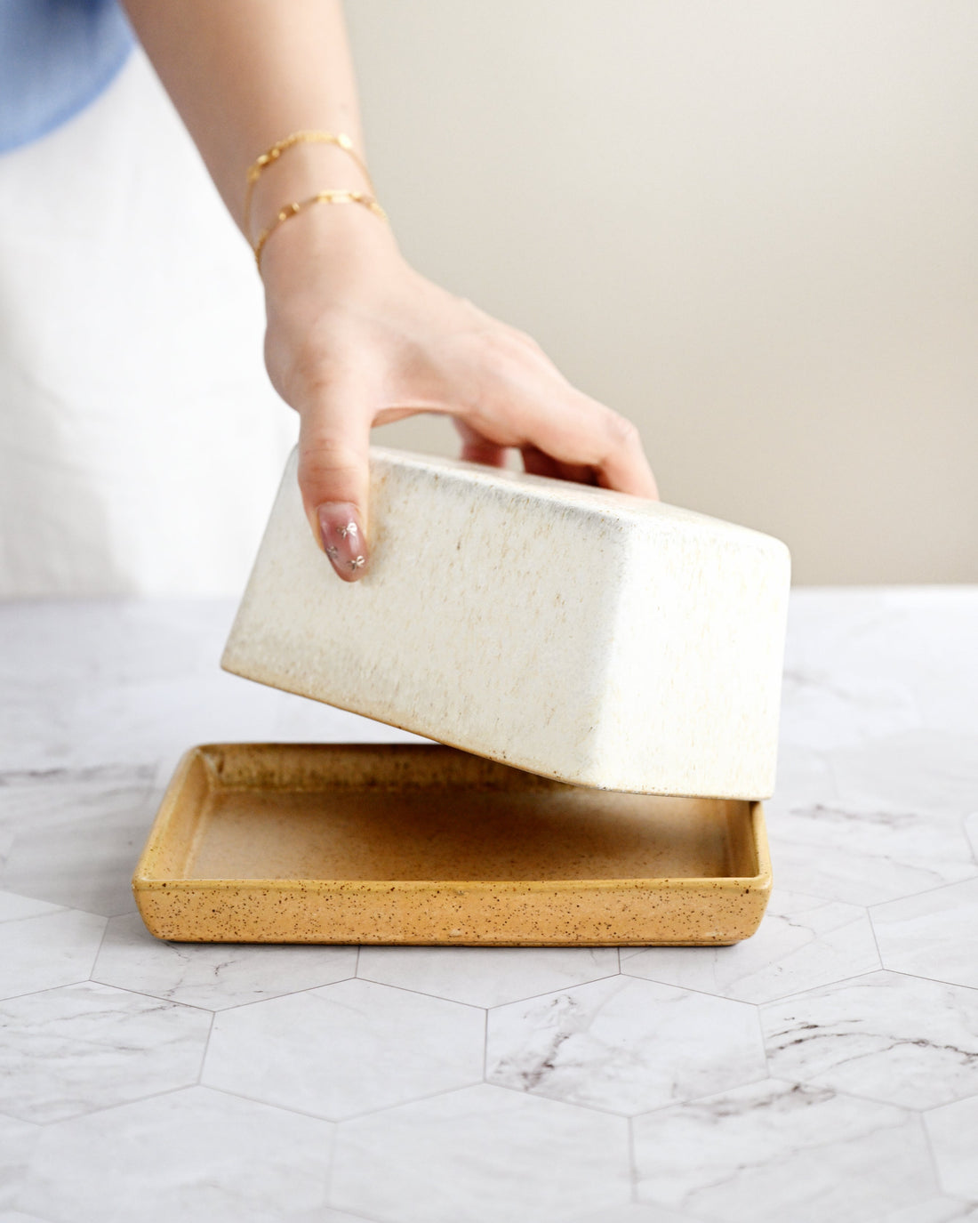 Person holding a white ceramic container over a wooden tray on a marble surface