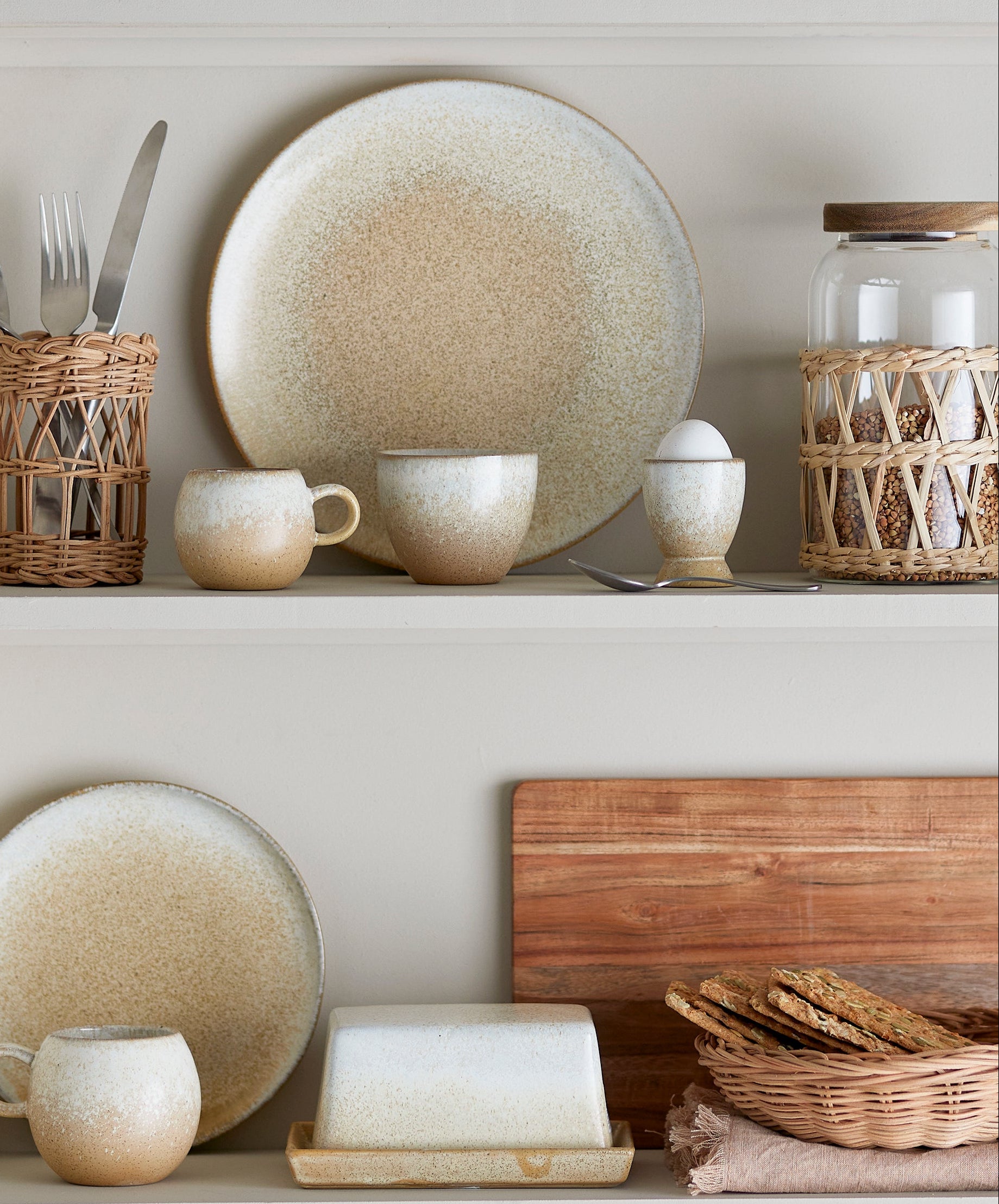Ceramic plates, mugs, and bowls on a shelf with wooden cutting board and bread.