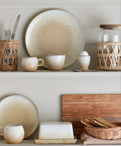 Ceramic plates, mugs, and bowls on a shelf with wooden cutting board and bread.