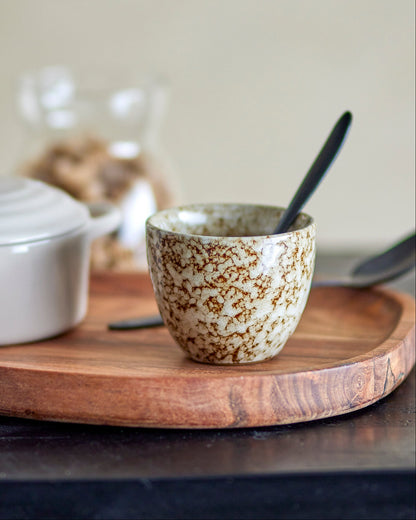 Ceramic mug with speckled pattern on a wooden tray with a neutral background