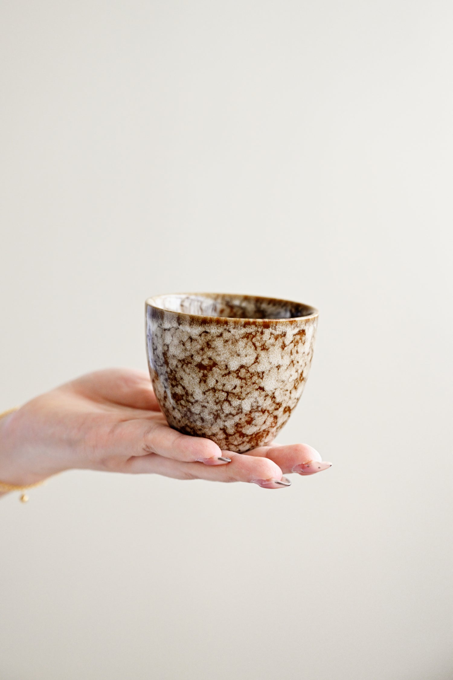 Hand holding a ceramic cup with a speckled design against a plain background