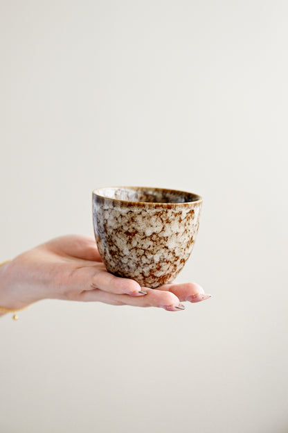 Hand holding a ceramic cup with a speckled design against a plain background