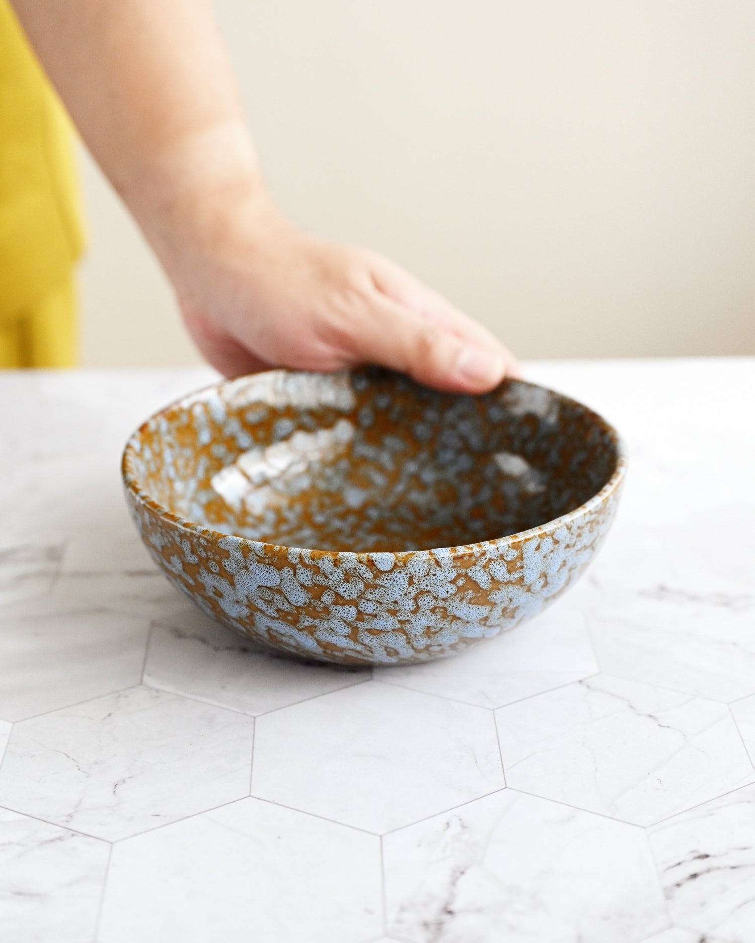 Person holding a ceramic bowl with a textured surface on a marble countertop