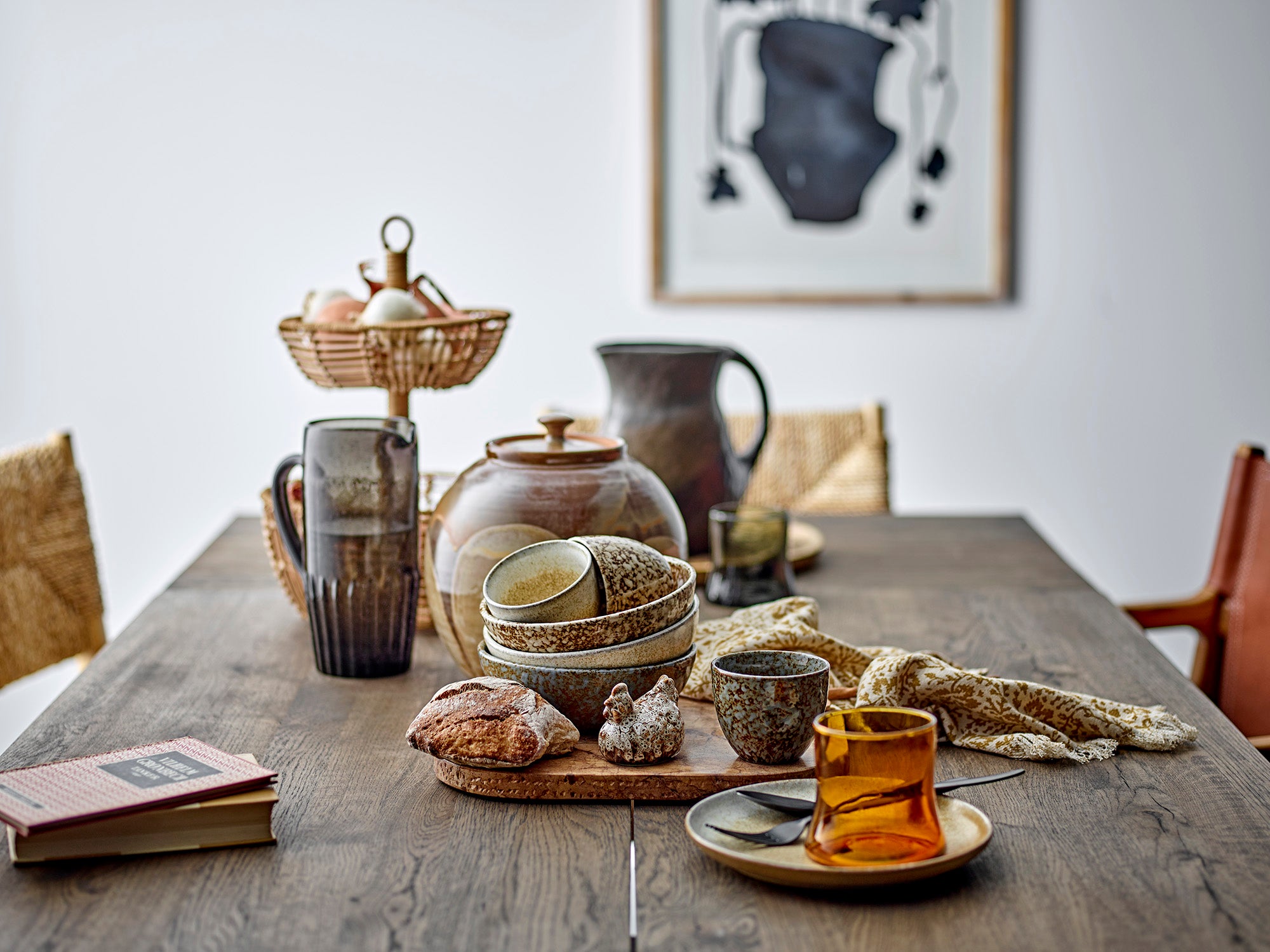 Dining table with rustic ceramic items, a teacup, and a book in a home setting.