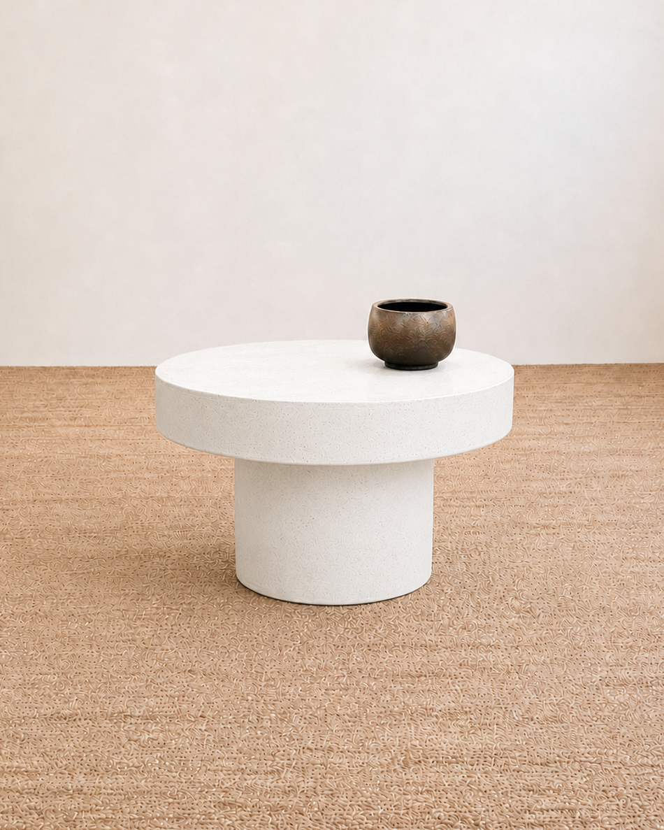 White round coffee table with a dark brown vase on a beige carpeted floor.
