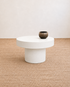 White round coffee table with a dark brown vase on a beige carpeted floor.