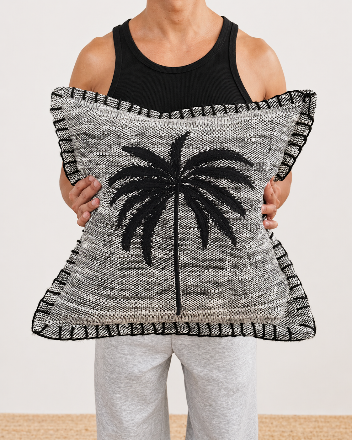 Person holding a decorative pillow with a palm tree design on a plain background
